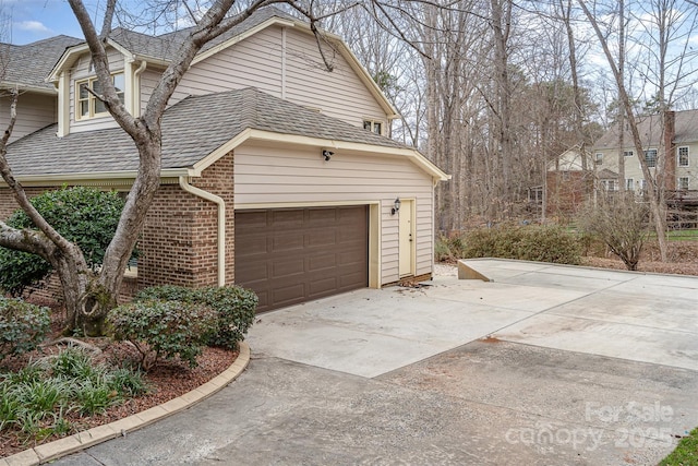 view of side of property featuring brick siding, driveway, and a shingled roof