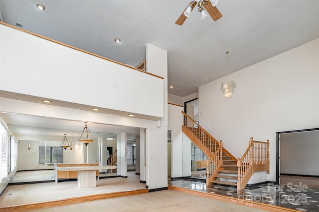 unfurnished living room with baseboards, ceiling fan, carpet, stairs, and a towering ceiling