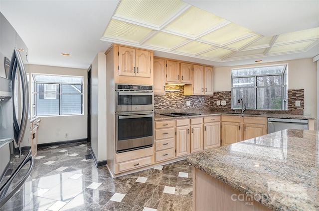 kitchen with light stone counters, light brown cabinets, stainless steel appliances, and a sink