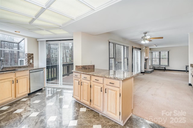 kitchen featuring light stone countertops, light brown cabinetry, stainless steel dishwasher, a ceiling fan, and a sink