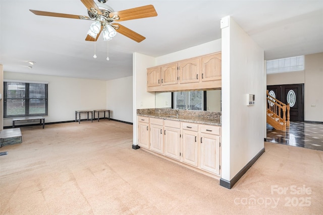 kitchen with light brown cabinetry, light carpet, baseboards, and light stone countertops