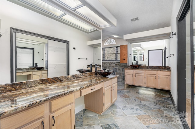 kitchen featuring visible vents, light brown cabinetry, dark stone counters, stone tile flooring, and a sink