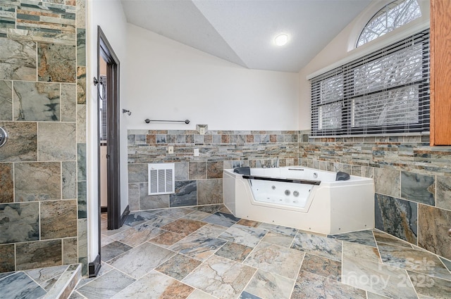 interior space featuring visible vents, a whirlpool tub, a tile shower, vaulted ceiling, and tile walls