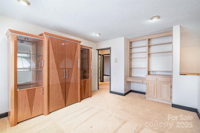 unfurnished bedroom featuring a textured ceiling, baseboards, light colored carpet, and built in study area