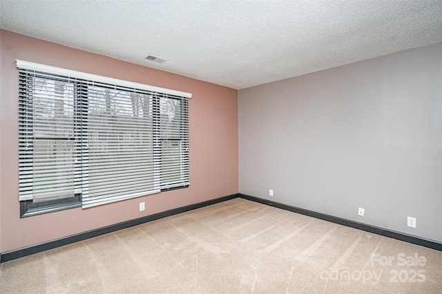 unfurnished room featuring baseboards, light colored carpet, visible vents, and a textured ceiling