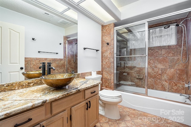 full bathroom with visible vents, combined bath / shower with glass door, toilet, and vanity