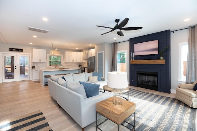 living room featuring visible vents, a large fireplace, recessed lighting, french doors, and light wood-style floors