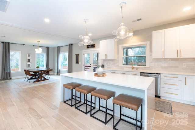 kitchen featuring stainless steel dishwasher, light countertops, light wood-style floors, and visible vents