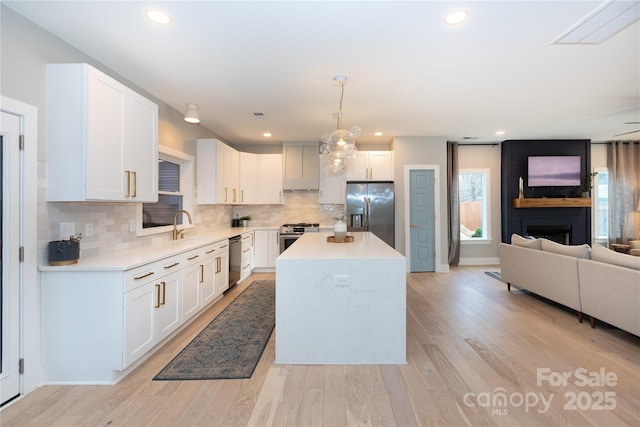 kitchen featuring stainless steel appliances, light wood-style floors, white cabinetry, open floor plan, and a large fireplace