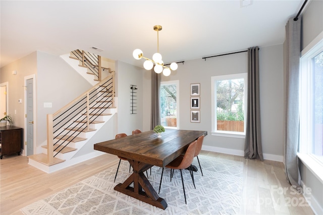 dining space featuring visible vents, a notable chandelier, light wood-style flooring, baseboards, and stairs