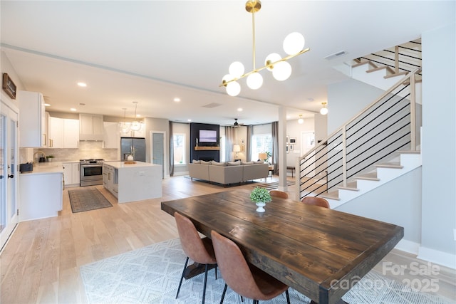 dining area featuring visible vents, light wood finished floors, baseboards, recessed lighting, and stairs