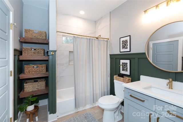 full bath featuring shower / bath combo with shower curtain, toilet, wainscoting, a decorative wall, and vanity