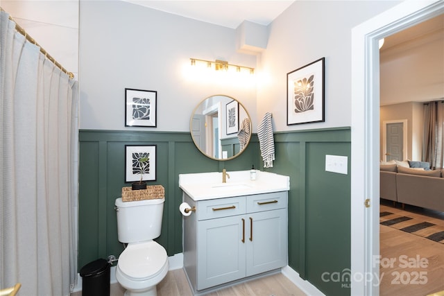 bathroom with toilet, wainscoting, wood finished floors, a decorative wall, and vanity