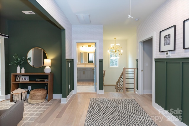 corridor with visible vents, light wood finished floors, a barn door, a notable chandelier, and an upstairs landing