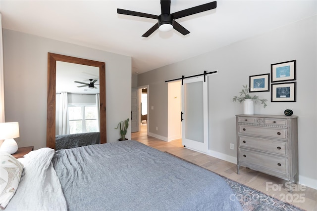 bedroom featuring ceiling fan, baseboards, light wood-style floors, and a barn door