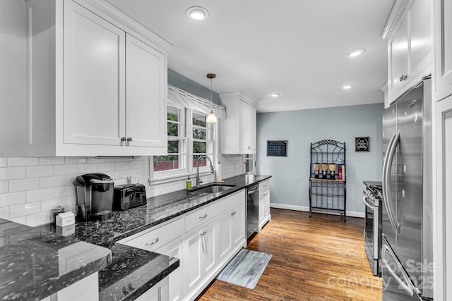 kitchen with a sink, backsplash, wood finished floors, stainless steel appliances, and white cabinets