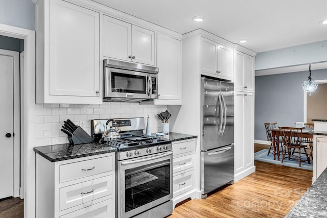 kitchen with decorative backsplash, white cabinetry, light wood-type flooring, and appliances with stainless steel finishes