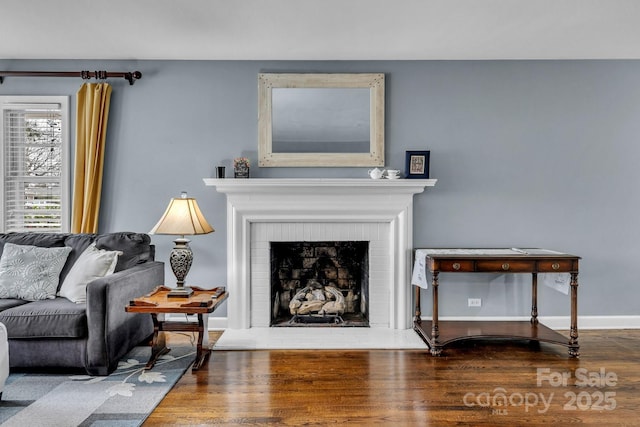 living room featuring a brick fireplace, wood finished floors, and baseboards