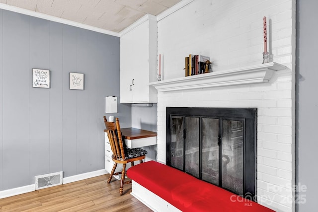 interior space with visible vents, wood finished floors, a fireplace, crown molding, and baseboards