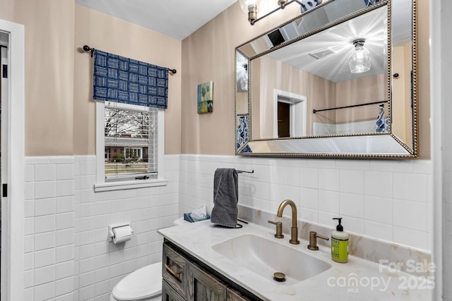 full bathroom featuring vanity, tile walls, toilet, and a wainscoted wall