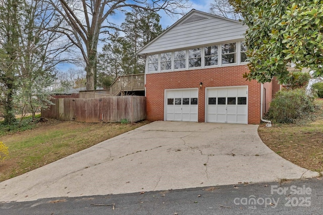 exterior space with fence, concrete driveway, a garage, brick siding, and stairs