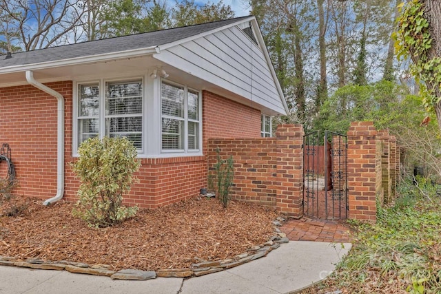 view of property exterior featuring brick siding and a gate