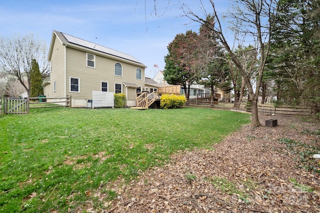 back of house featuring a wooden deck, roof mounted solar panels, a lawn, metal roof, and a fenced backyard