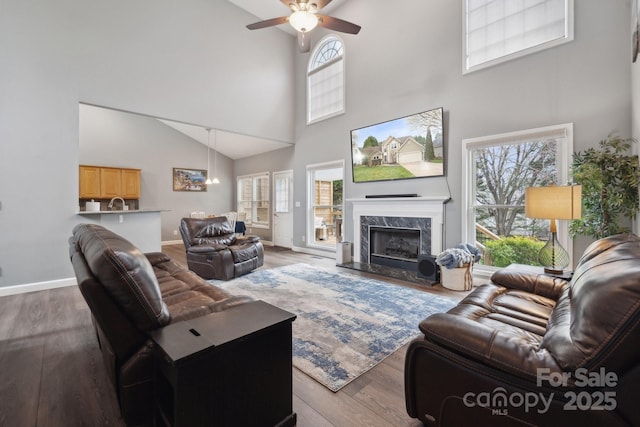 living room with a fireplace, wood finished floors, baseboards, and a ceiling fan