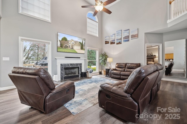 living room with wood finished floors, a towering ceiling, a fireplace, baseboards, and ceiling fan