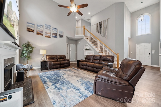 living area featuring wood finished floors, baseboards, a fireplace, stairs, and a towering ceiling