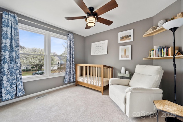 carpeted bedroom featuring visible vents, baseboards, a nursery area, and a ceiling fan