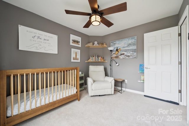 bedroom featuring baseboards, a nursery area, a ceiling fan, and carpet