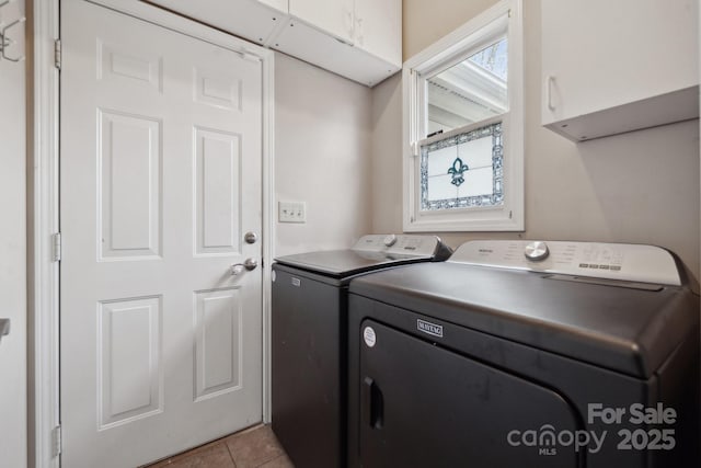 clothes washing area featuring washer and dryer, light tile patterned flooring, and cabinet space