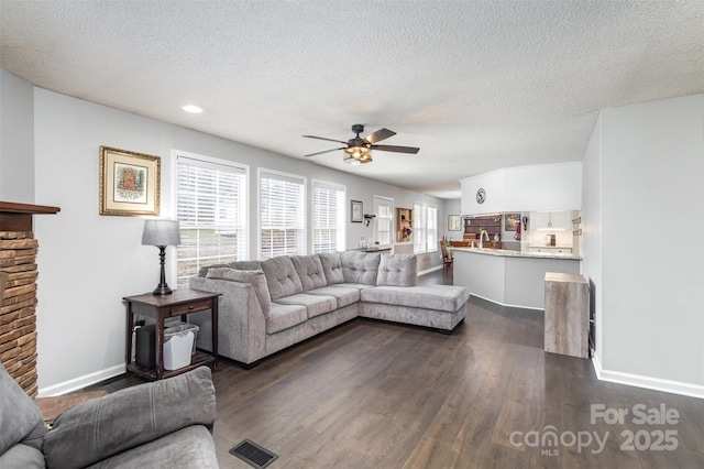 living room featuring visible vents, dark wood-type flooring, baseboards, ceiling fan, and a textured ceiling