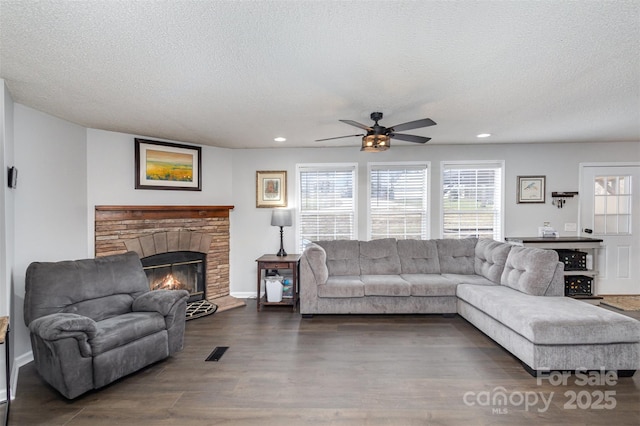 living room featuring wood finished floors, visible vents, ceiling fan, a stone fireplace, and a textured ceiling