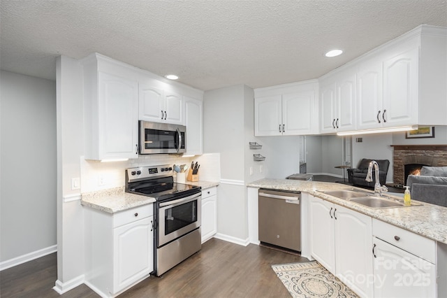 kitchen featuring dark wood finished floors, a warm lit fireplace, a sink, stainless steel appliances, and white cabinetry