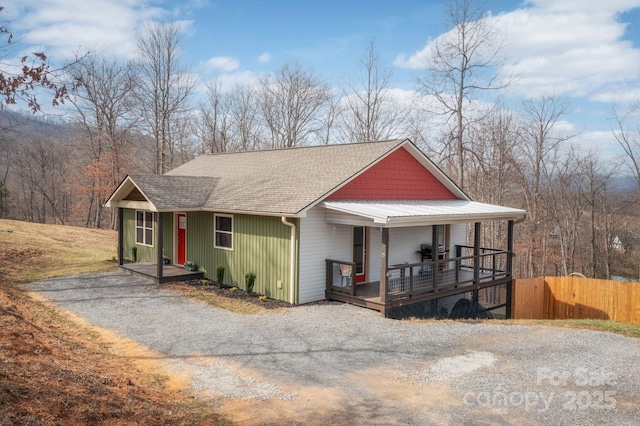view of front facade featuring gravel driveway, roof with shingles, covered porch, and fence
