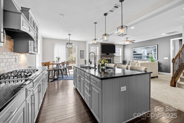 kitchen with visible vents, a stone fireplace, gray cabinets, a ceiling fan, and a sink