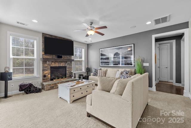 living room featuring baseboards, visible vents, a stone fireplace, and ceiling fan