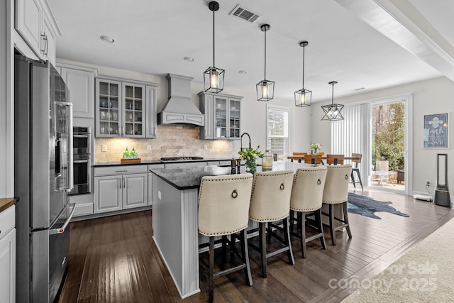 kitchen with tasteful backsplash, visible vents, premium range hood, a breakfast bar area, and stainless steel appliances