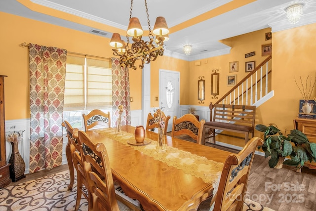 dining room with a wainscoted wall, ornamental molding, wood finished floors, a chandelier, and stairs