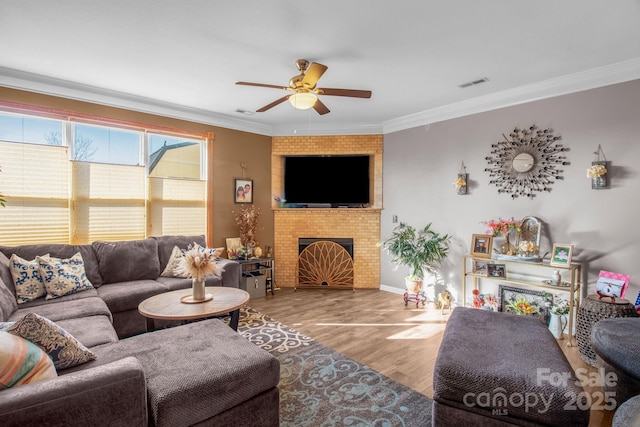 living room with visible vents, a ceiling fan, wood finished floors, a fireplace, and crown molding