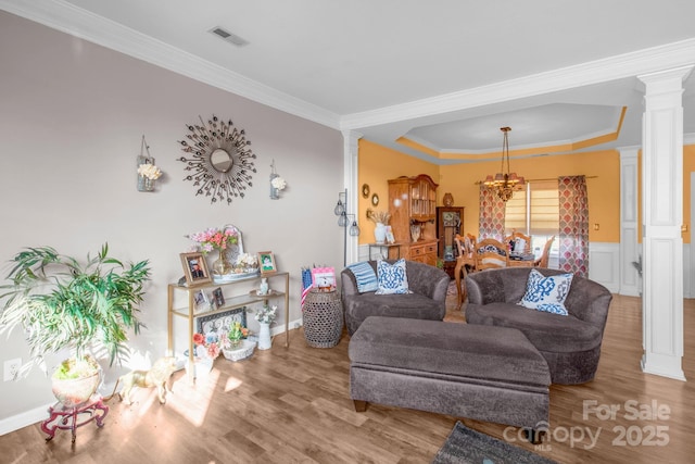 living area featuring crown molding, wood finished floors, a tray ceiling, and ornate columns