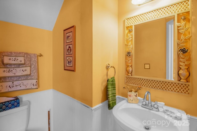 half bath featuring lofted ceiling, toilet, a wainscoted wall, and a sink