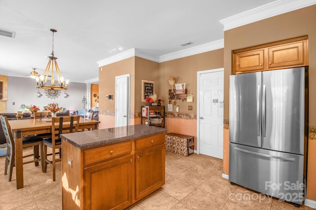 kitchen with visible vents, a kitchen island, dark countertops, freestanding refrigerator, and a chandelier