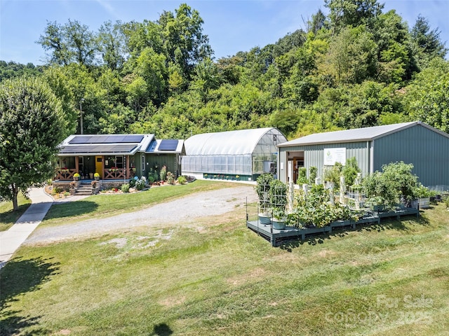 view of front of home featuring an outbuilding, a front lawn, roof mounted solar panels, an exterior structure, and a garden