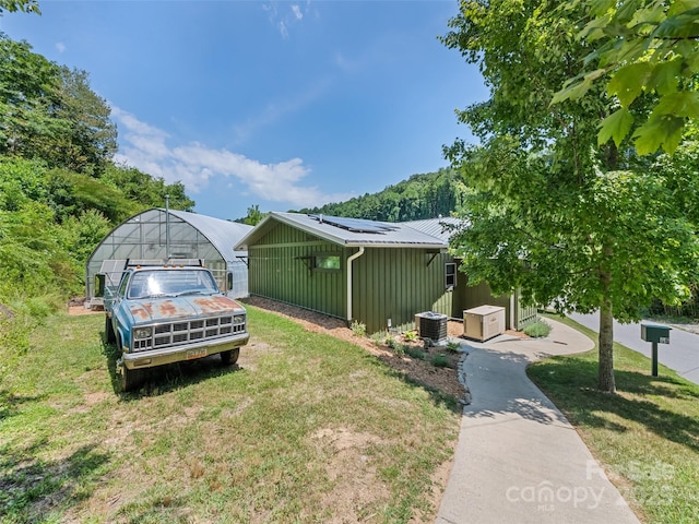 exterior space with an exterior structure, an outdoor structure, central air condition unit, a lawn, and metal roof