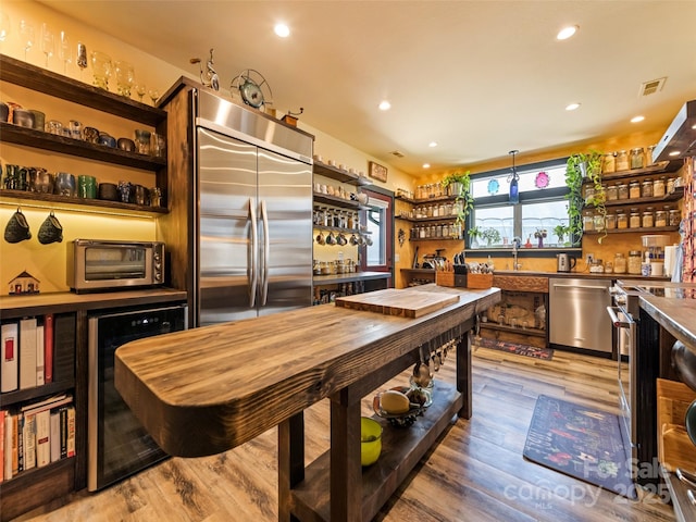 kitchen featuring beverage cooler, a toaster, wood finished floors, stainless steel appliances, and open shelves