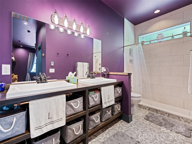 full bath featuring double vanity, toilet, tiled shower, and a sink