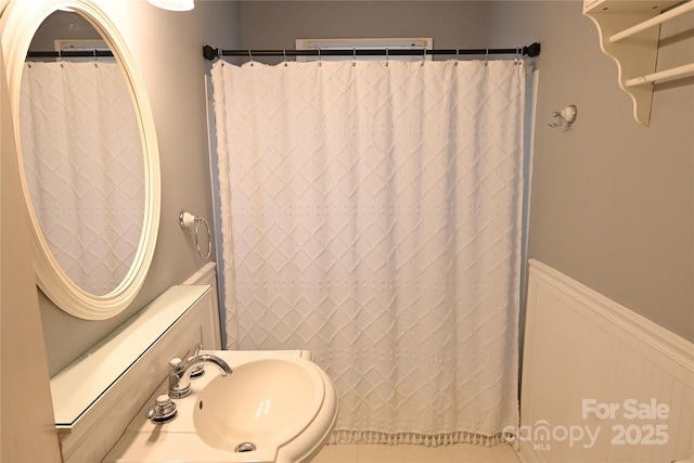 bathroom featuring a wainscoted wall, a shower with shower curtain, and a sink